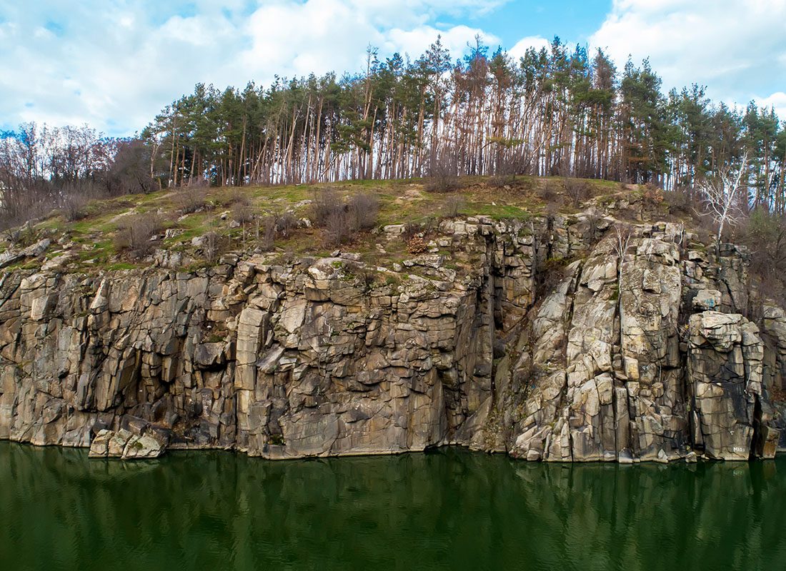 Barre, VT - Aerial View of a Rocky Ledge With Pine Trees and a Lake Below